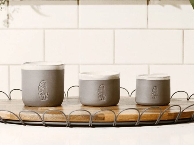 Three gray ceramic cups with embossed La Marzocco logo on a wooden tray with metal handles