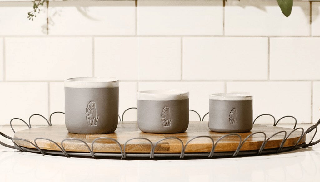 Three gray ceramic cups with embossed La Marzocco logo on a wooden tray with metal handles