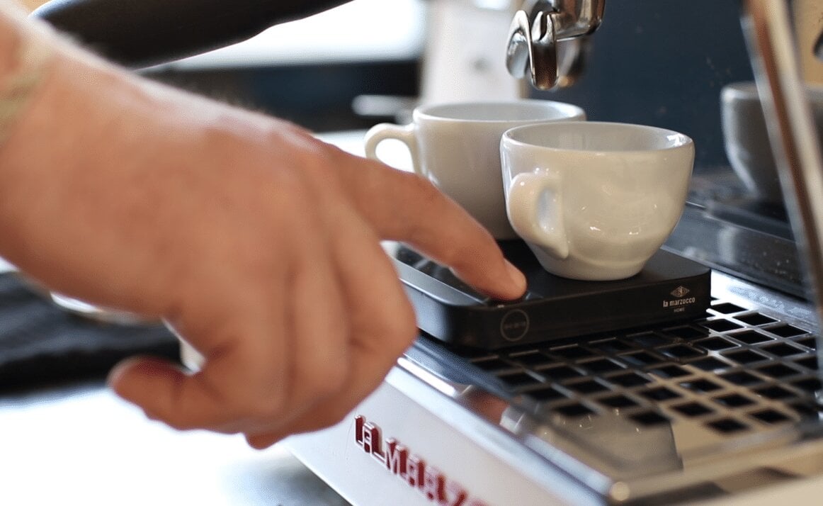 Pouring espresso with La Marzocco espresso machine and white ceramic cups on desk