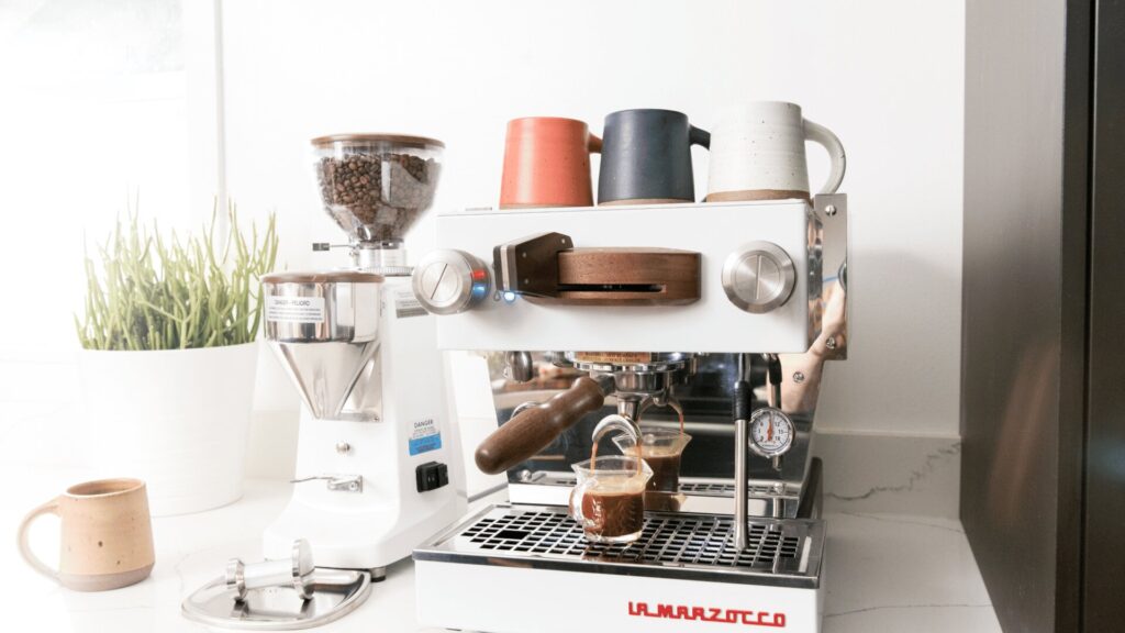 La Marzocco espresso machine and grinder setup with accessories on white shelf
