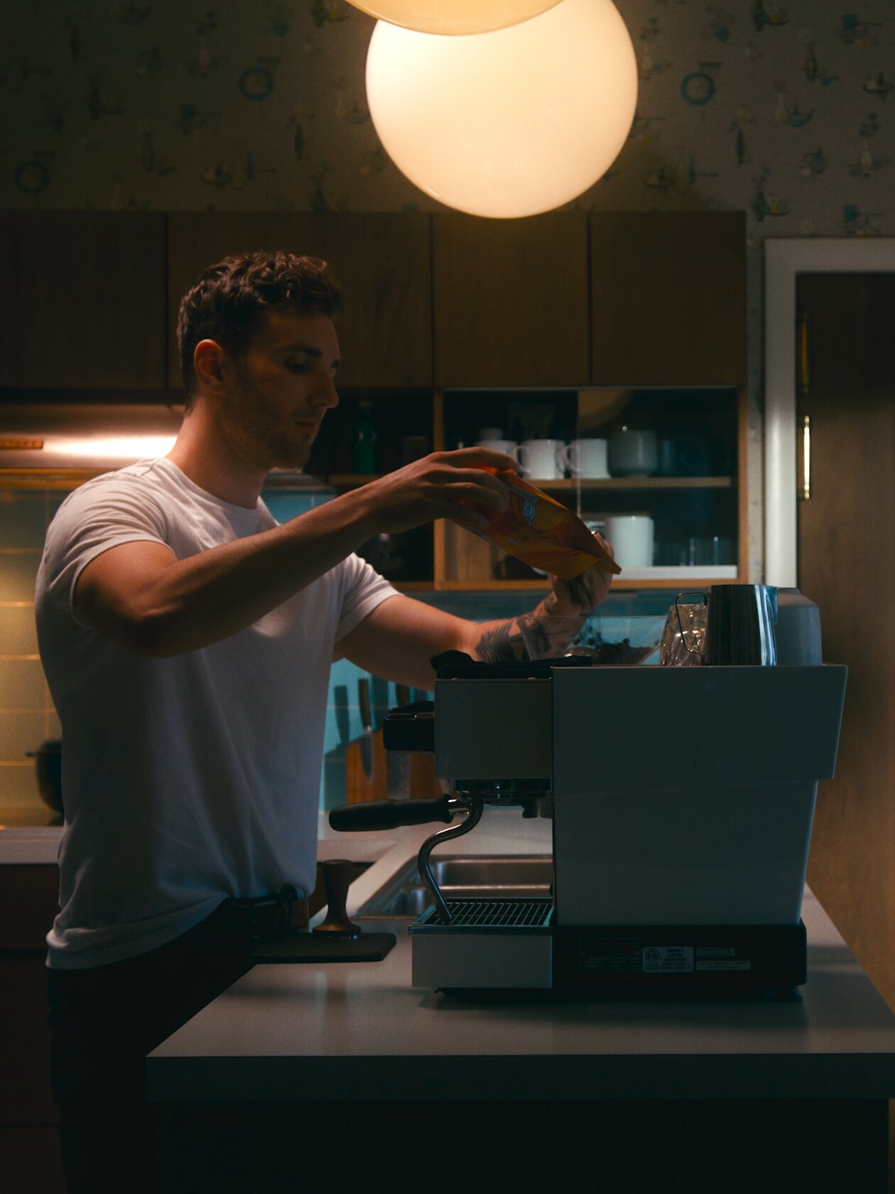 Man using a La Marzocco espresso machine in a modern kitchen with warm lighting