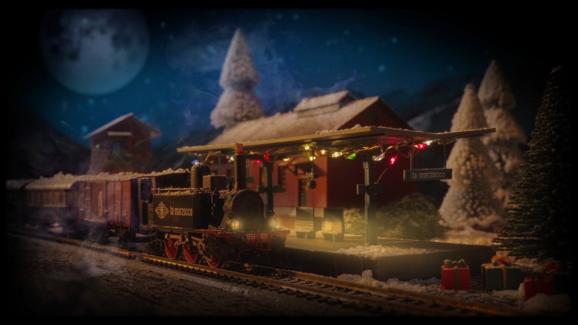 Miniature train with holiday lights at a snowy station beneath a full moon