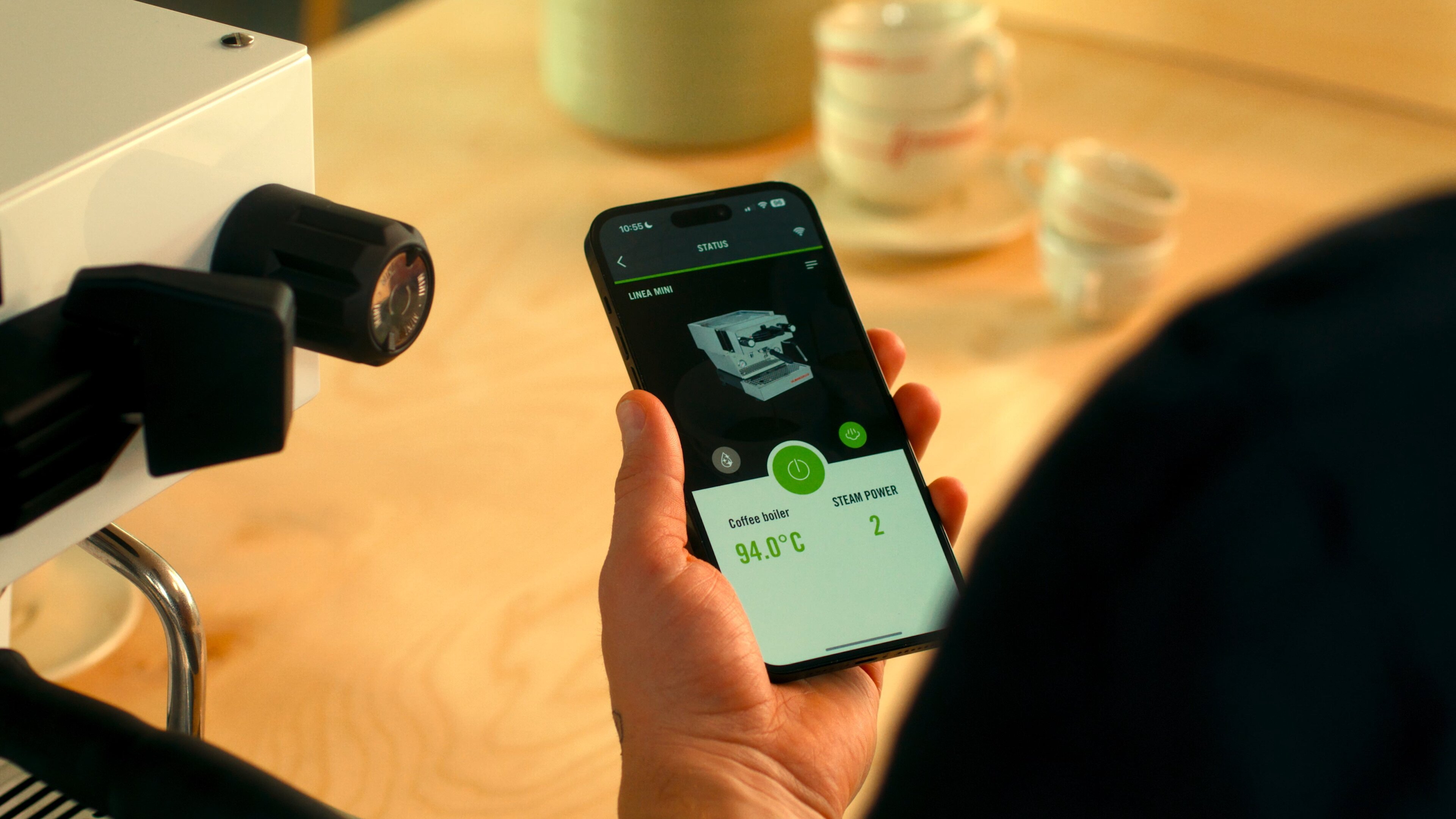 Person holding a smartphone displaying the La Marzocco app with a Linea Mini espresso machine, showing steam power control at 94.0°C