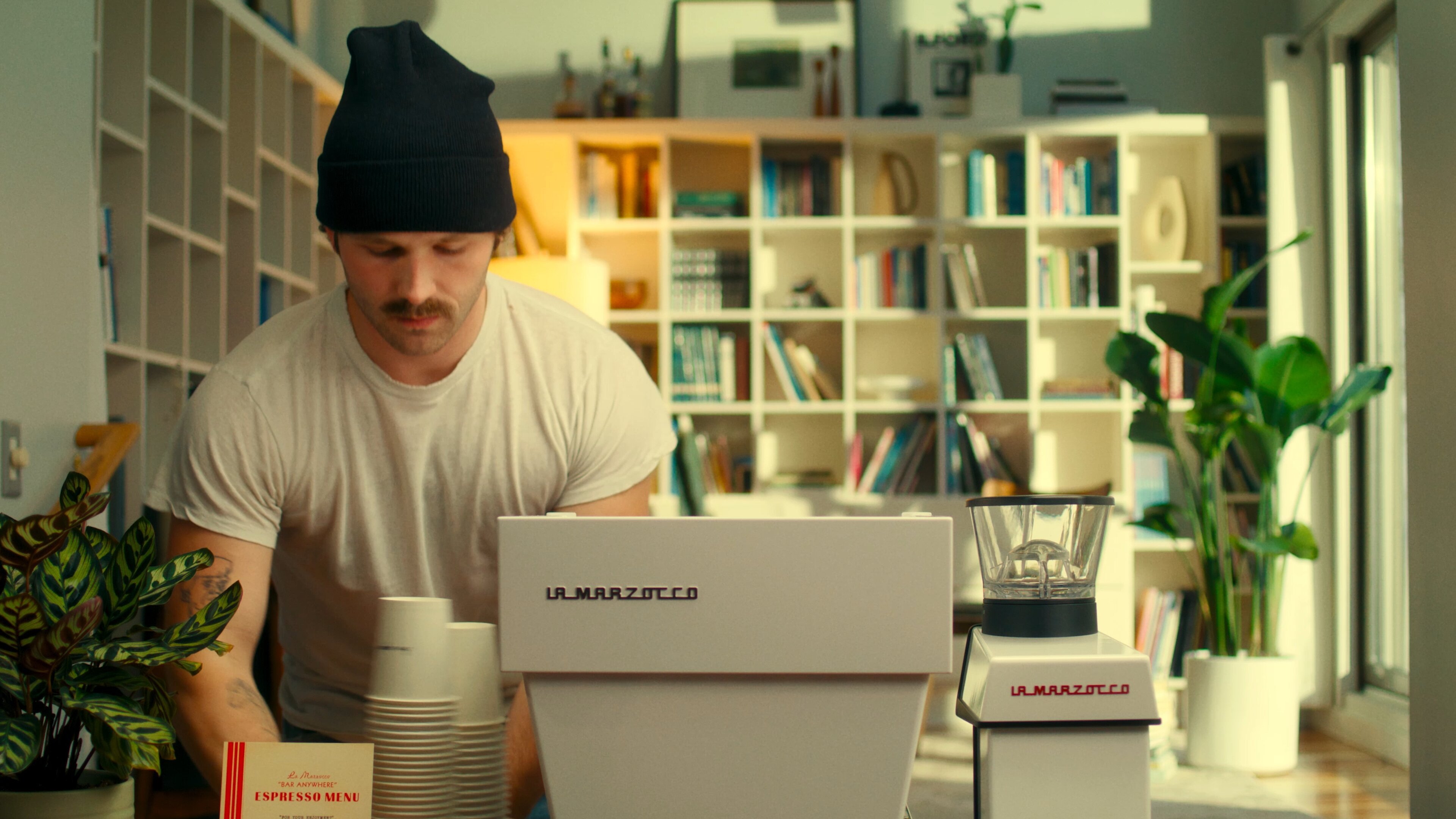 Man setting up a La Marzocco Linea Mini espresso machine at a pop-up bar in a modern home kitchen with bookshelves