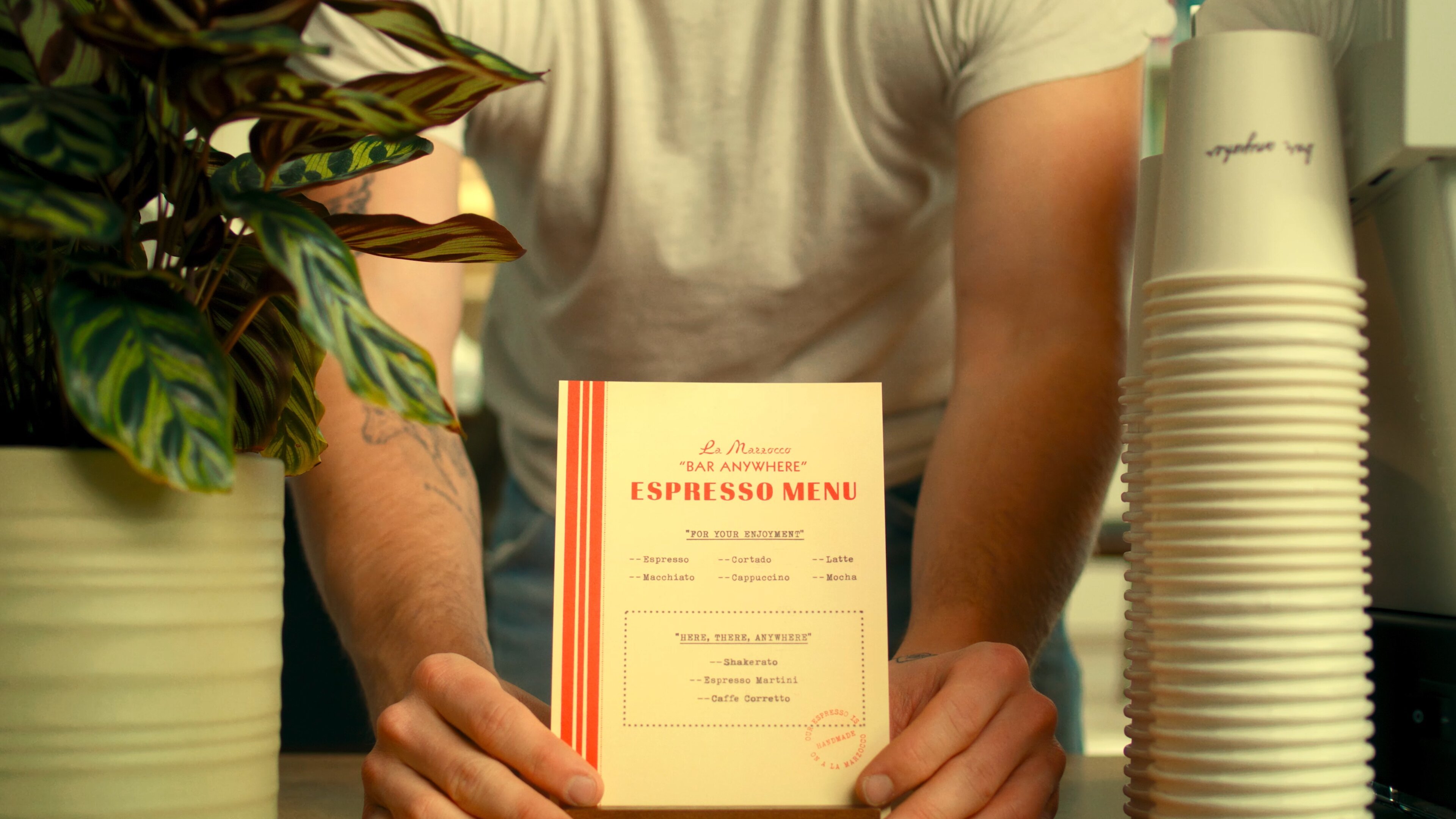 La Marzocco Linea Mini espresso menu guide held in hands with coffee cups and plant in background