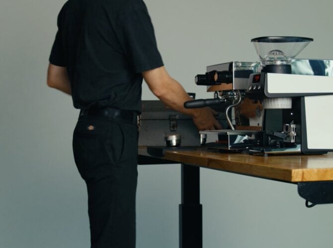 Barista operating a La Marzocco espresso machine at a wooden counter