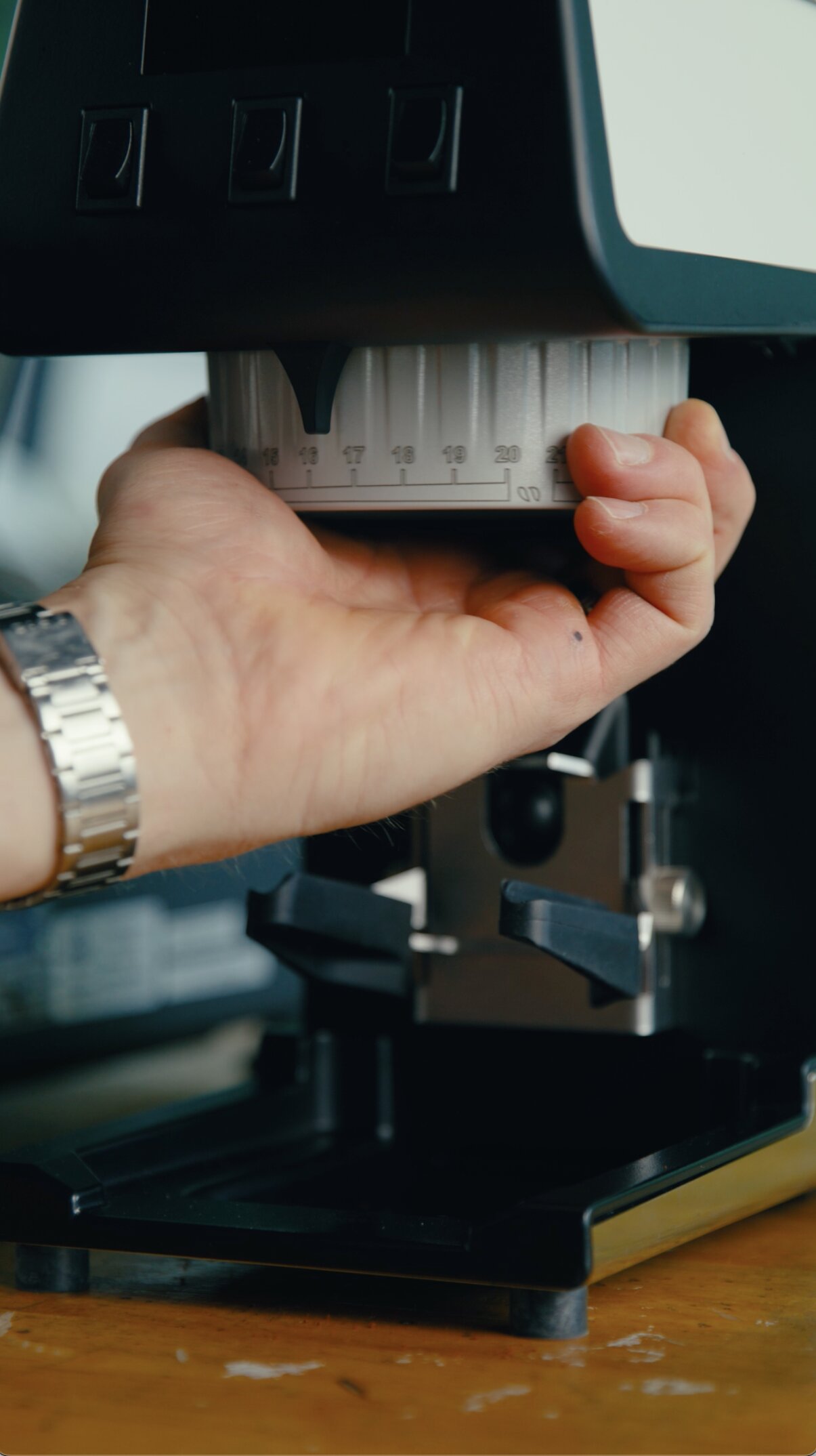 Hands holding a measuring ruler against a La Marzocco espresso machine group head, demonstrating machine dimensions