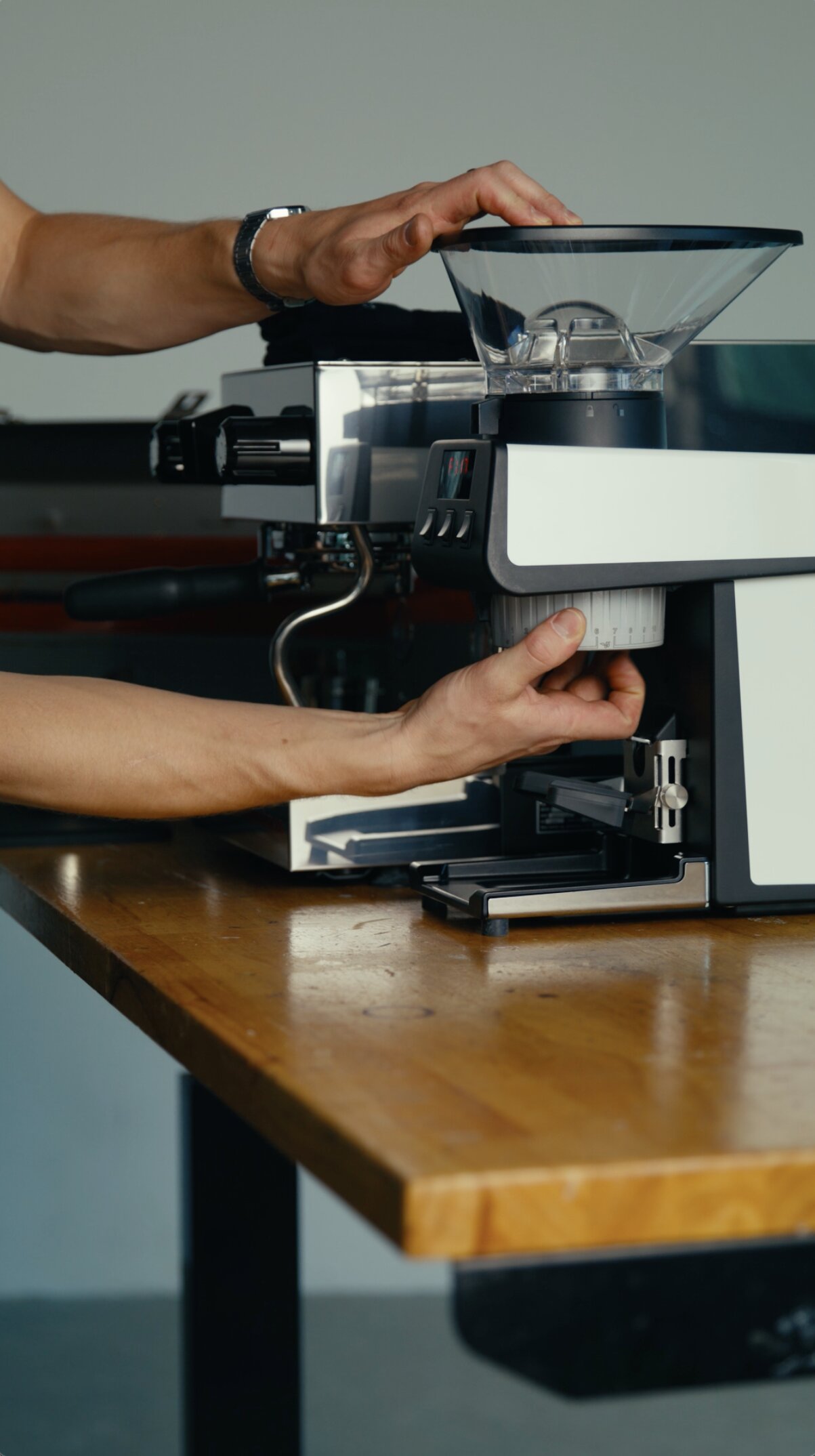Hand operating the portafilter on a La Marzocco espresso machine, demonstrating the group head and machine features on a wooden table