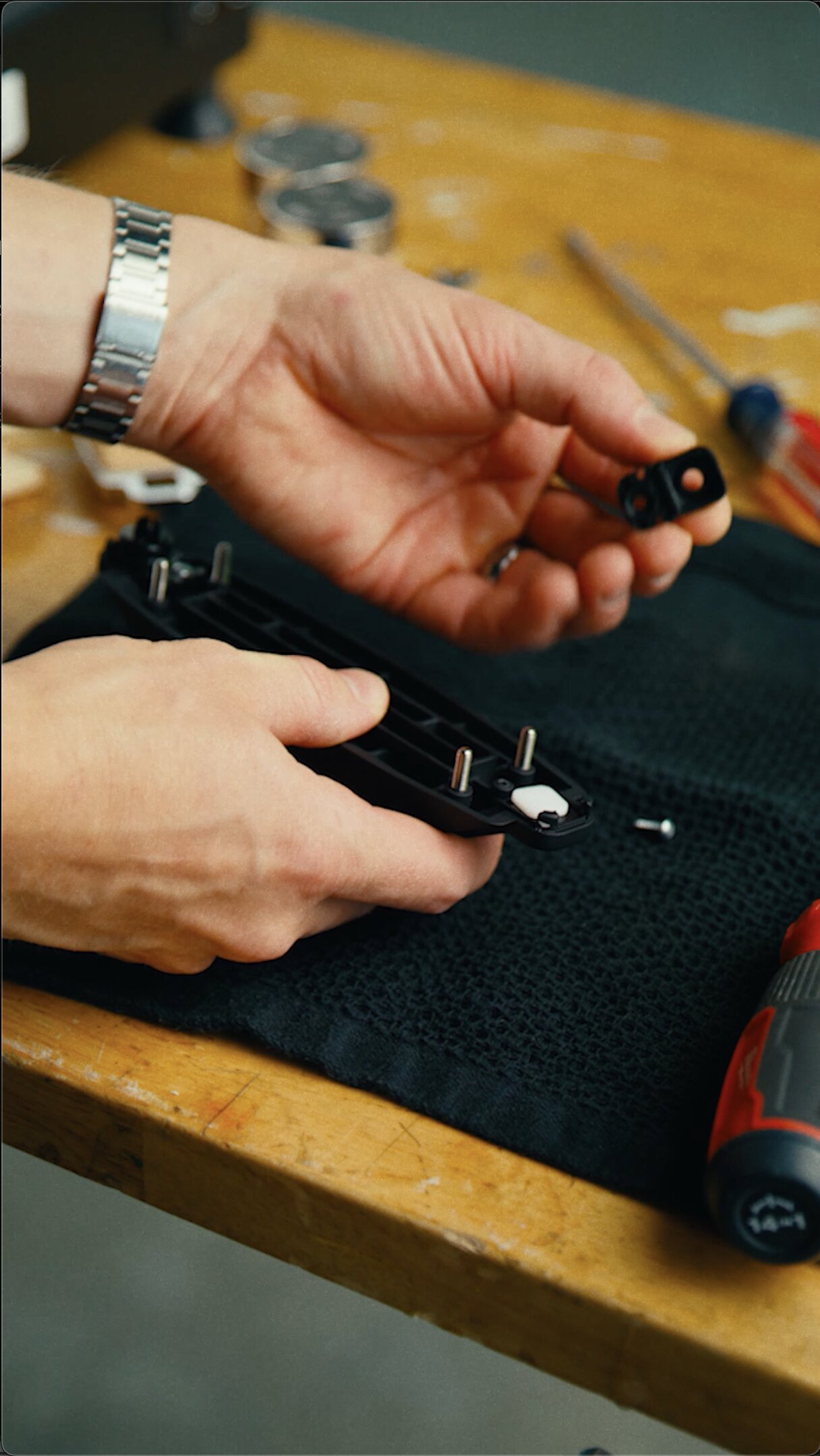 Hands holding La Marzocco espresso machine portafilter and group head assembly on wooden table with grinder in background