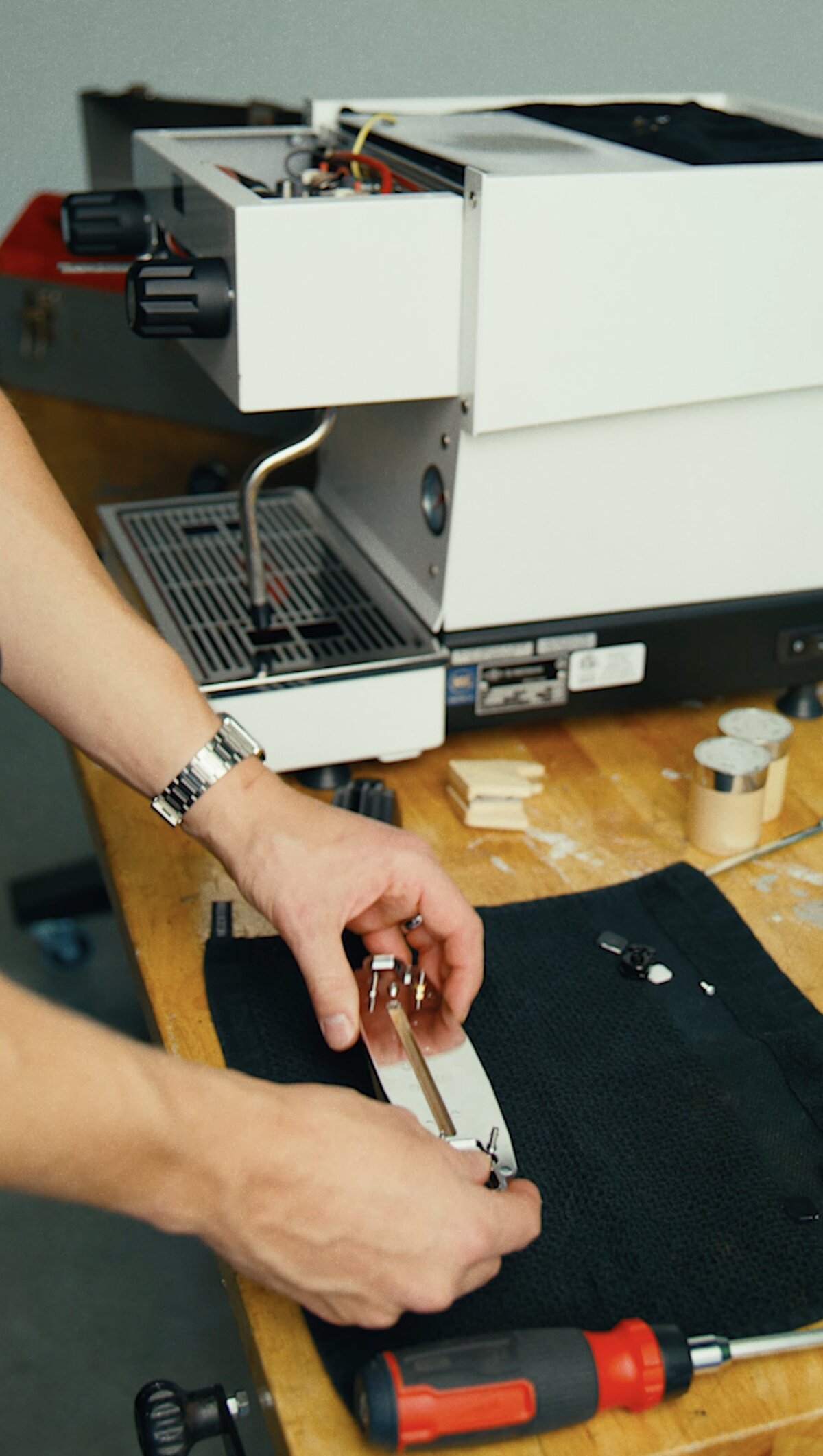 Hands assembling a La Marzocco espresso machine component on a wooden work surface