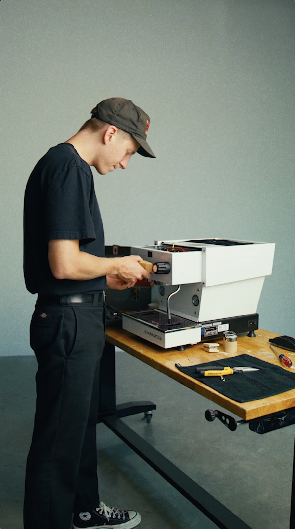 Technician performing maintenance on a La Marzocco espresso machine at a wooden workbench with tools