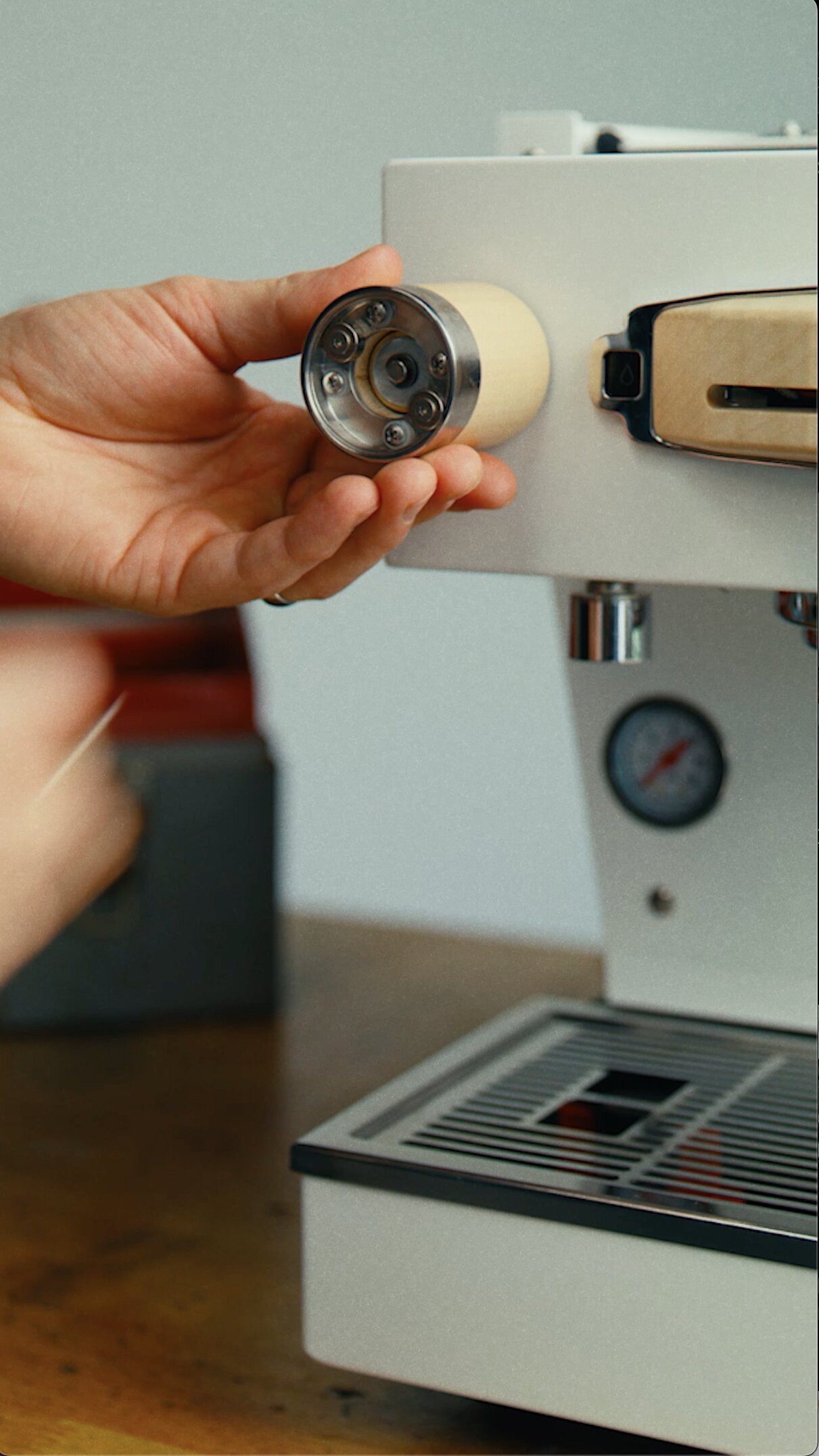 Hand holding La Marzocco espresso machine group head with shower screen and dispersion plate visible, installed on white espresso machine body