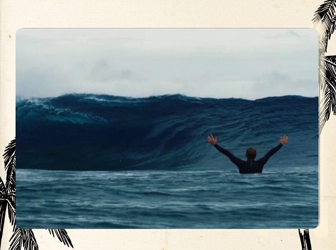 Person in water with arms raised facing large ocean waves