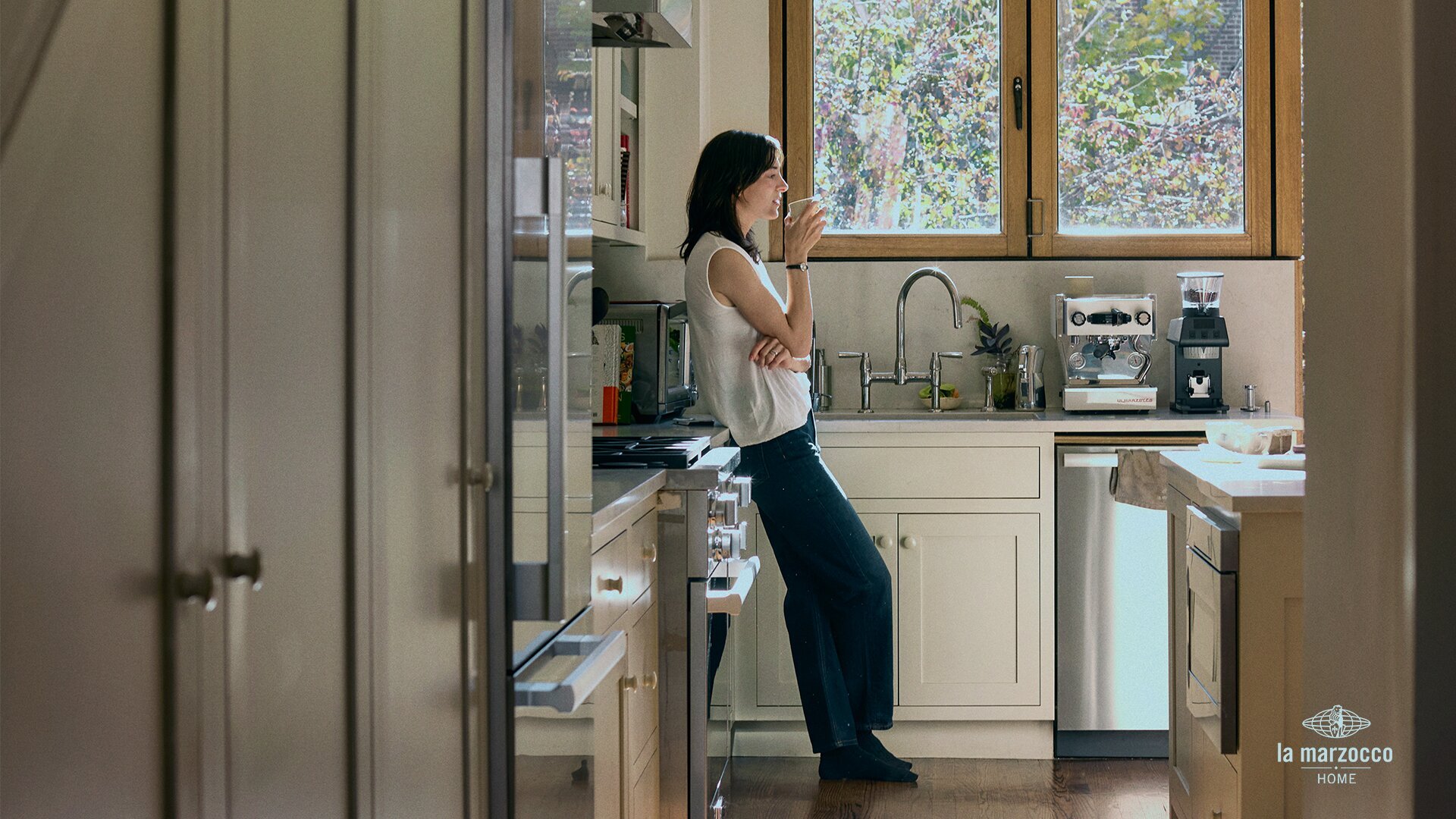 Woman taking a sip of espresso in a modern kitchen with La Marzocco espresso machine and grinder on the countertop