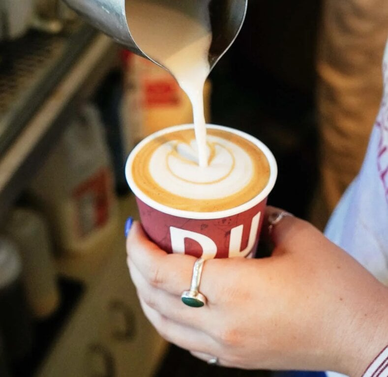 Barista pouring steamed milk into espresso with latte art in a red cup
