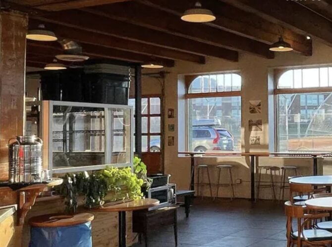 Interior of a specialty coffee shop with La Marzocco espresso machine, wooden counter, large windows, and seating area