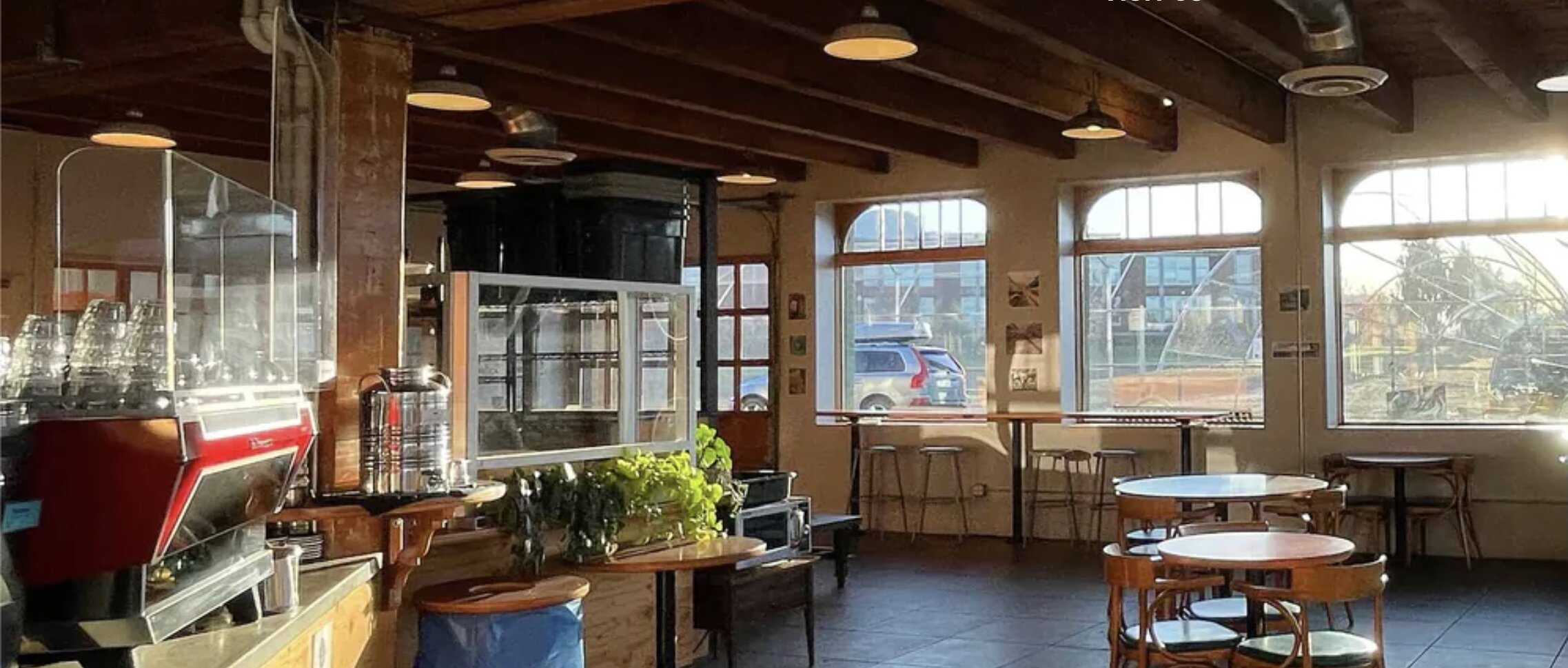 Interior of a specialty coffee shop with La Marzocco espresso machine, wooden counter, large windows, and seating area