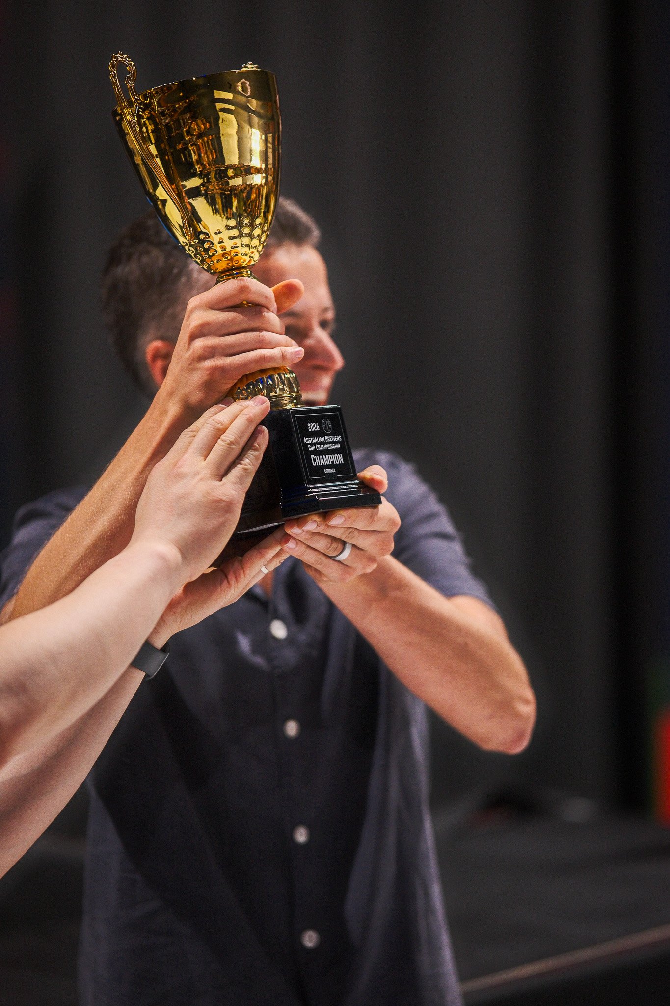 Person holding a gold trophy cup with a black base engraved with "Champion"